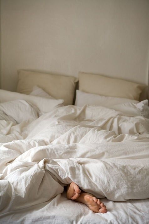 a person laying in bed with white sheets and blankets on it's sides, their feet sticking out from under the covers