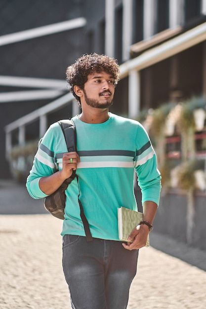 a man walking down the street with a book in his hand and a backpack on his shoulder