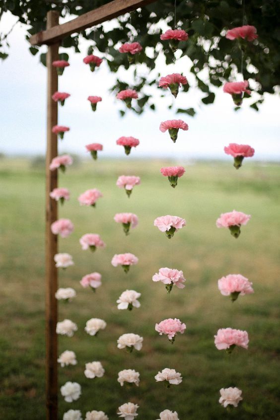 pink and white carnations are hanging from a wooden pole in the middle of a field