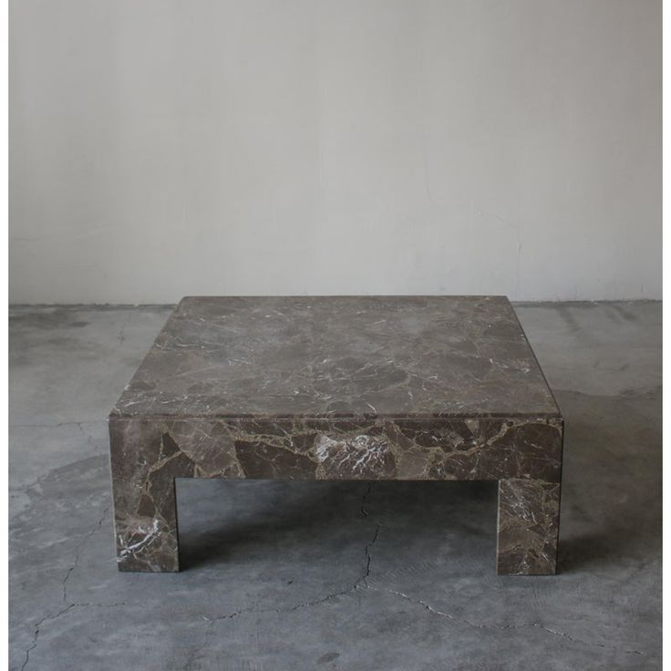 a marble coffee table sitting on top of a cement floor next to a white wall