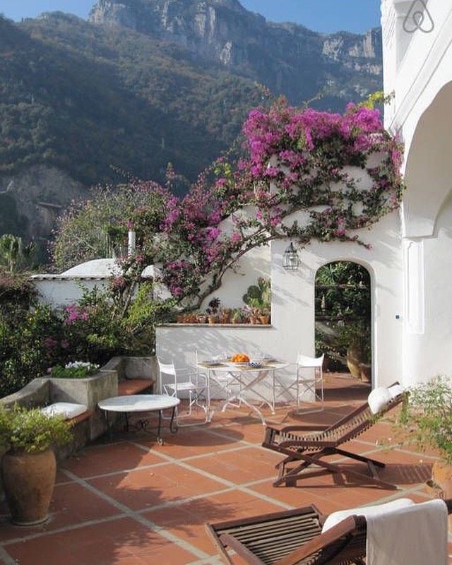 an outdoor patio with chairs, tables and flowers on the wall next to mountains in the background