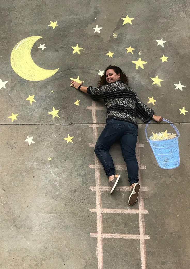 a woman laying on top of a ladder drawing stars and moon