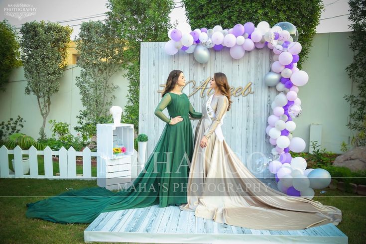 two women standing next to each other in front of a backdrop with balloons and streamers