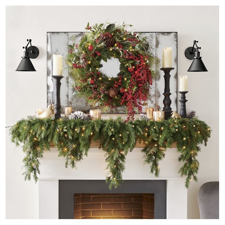 a christmas mantle decorated with greenery, pine cones and candles next to a wreath