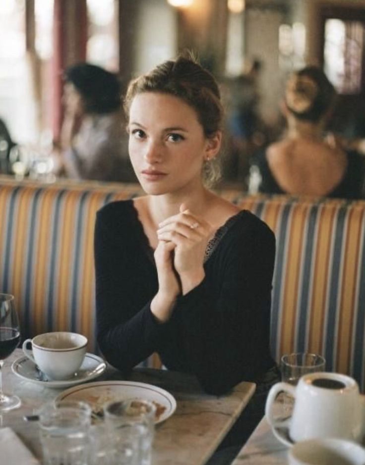 a woman sitting at a table in a restaurant with her hands clasped to her chest