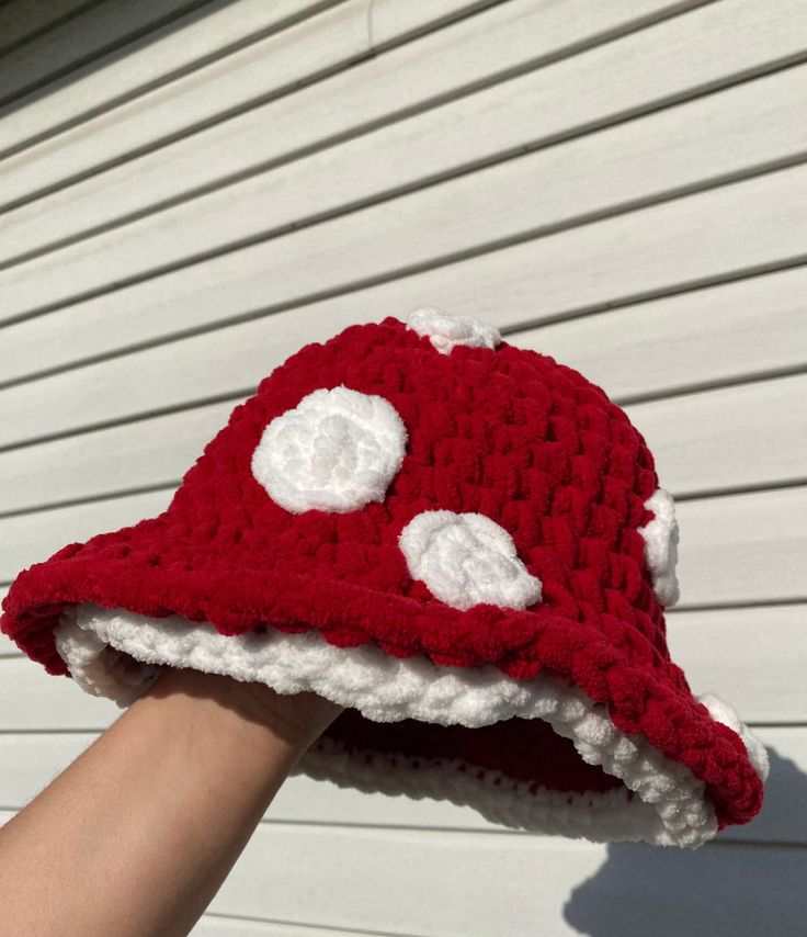 someone is holding up a crocheted red and white hat that looks like a mushroom