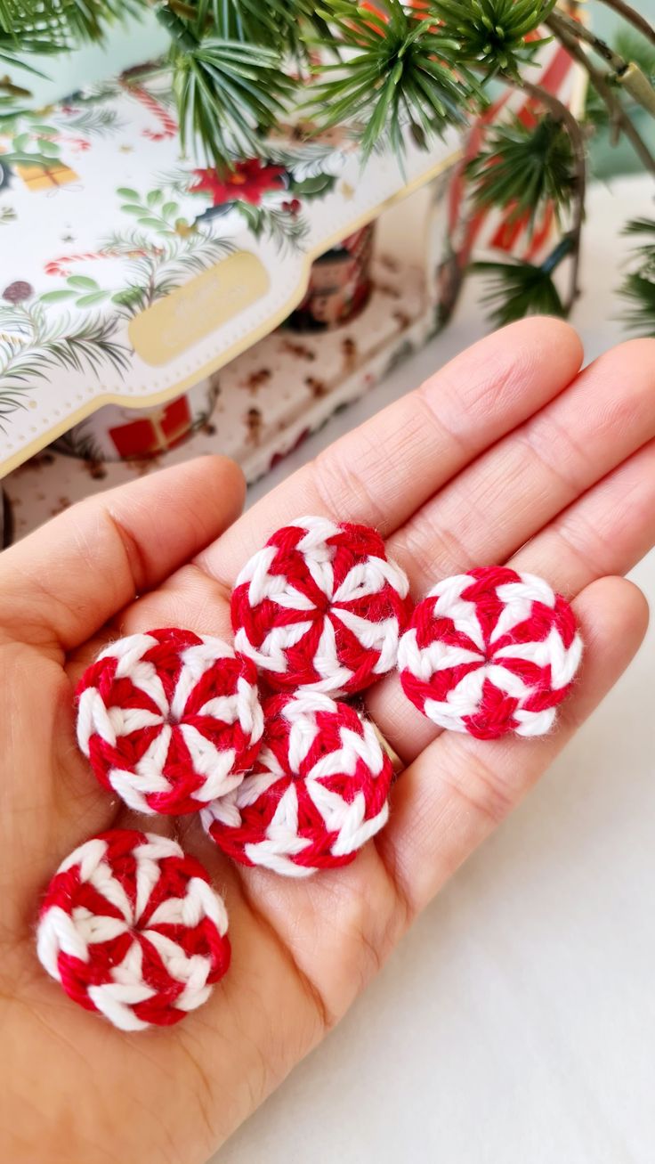 four red and white fabric buttons sitting in someone's hand next to christmas tree