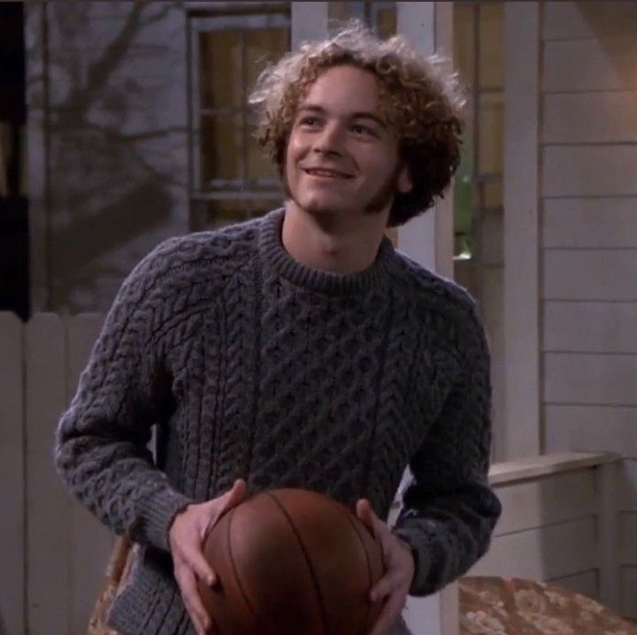 the young man is holding a basketball in his right hand and smiling at the camera