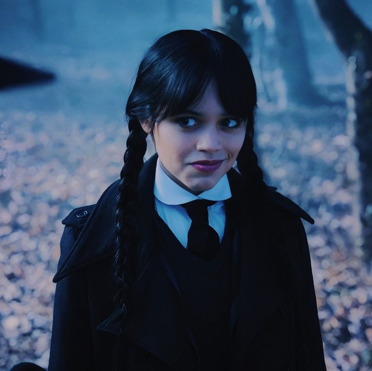 a woman with long hair wearing a black coat and tie in the woods, looking at the camera