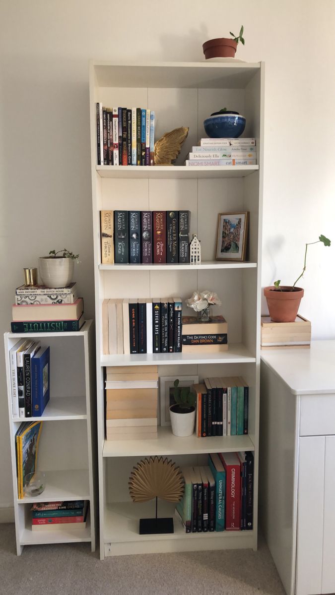 a bookshelf filled with lots of books next to a white desk and chair