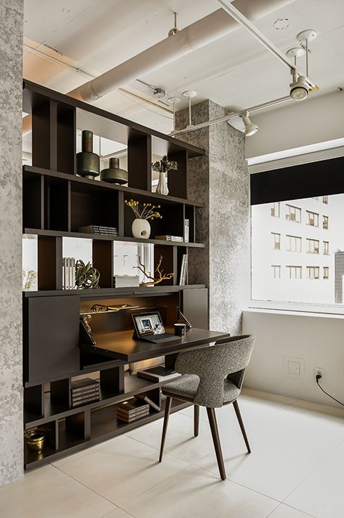 a room with a desk, chair and bookcases on the wall in front of a window