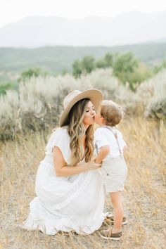 a woman in white dress and hat holding a small child on her lap while standing in tall grass