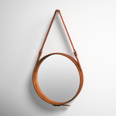 a round mirror hanging on the wall next to a leather strap with a wooden handle