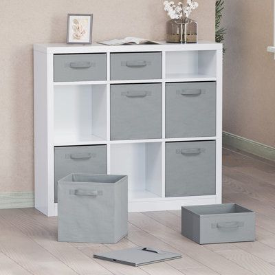 a white bookcase with grey bins and two gray boxes on the floor next to it