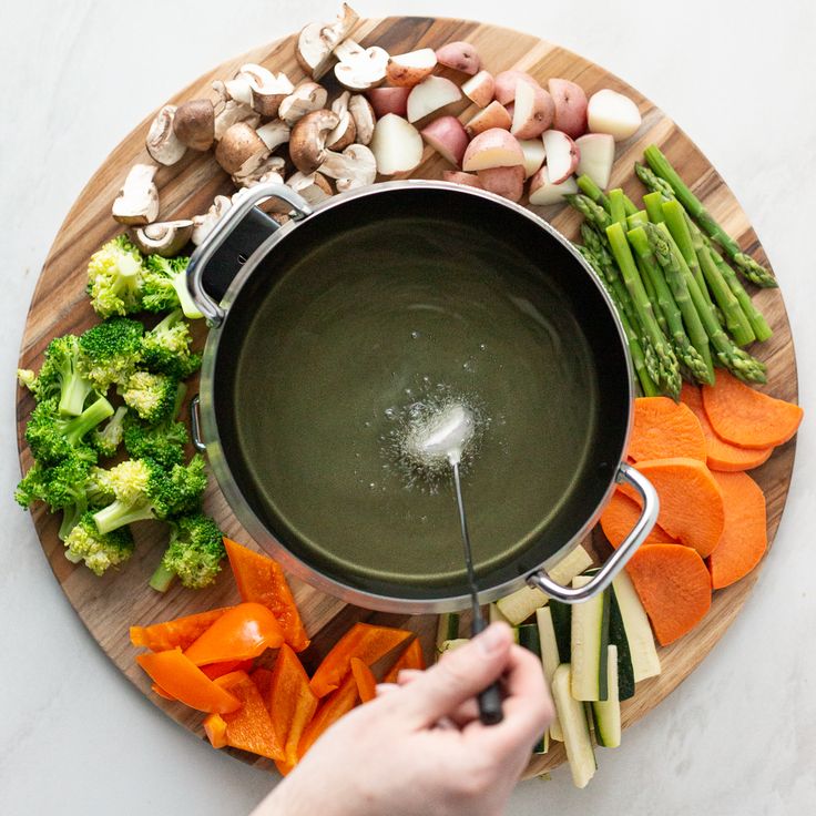 a person is stirring broth in a pot on a cutting board with vegetables and mushrooms