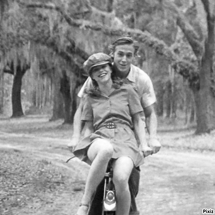 a man and woman riding on the back of a motorcycle down a dirt road with trees in the background