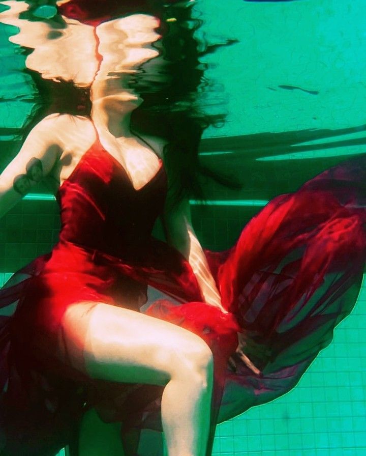 a woman in a red dress sitting on the side of a swimming pool