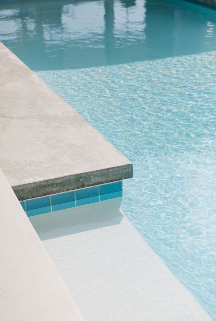 an empty swimming pool with blue water and white tiles on the edge is pictured in this image