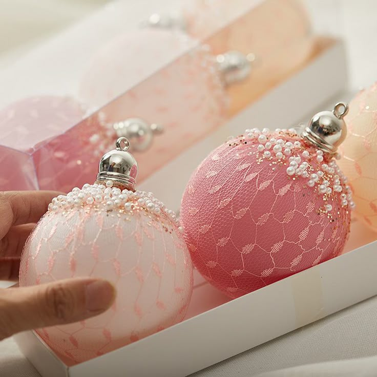 two pink and white christmas ornaments in a box with a person's hand reaching for one