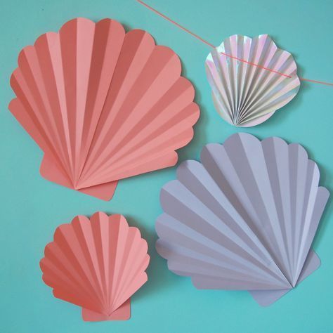 three seashells hanging on a string against a blue background, one is pink and the other is lilac