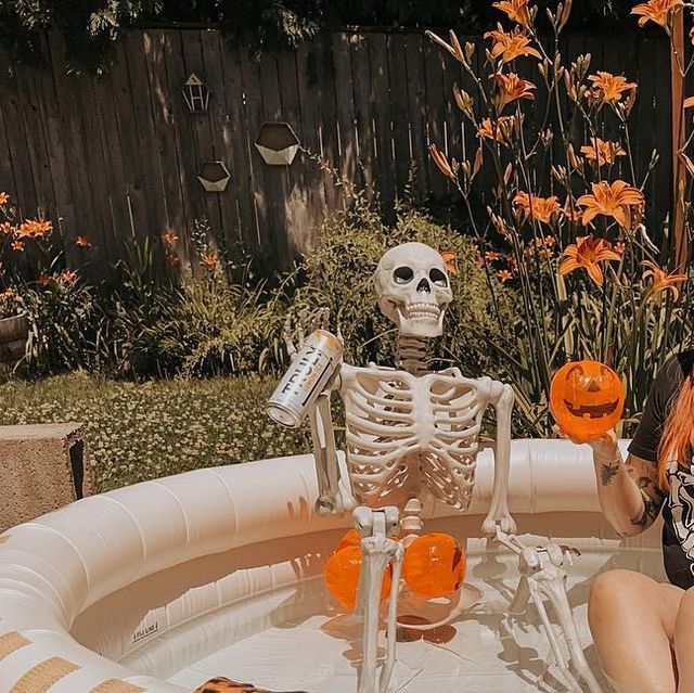 a woman sitting in an inflatable pool with a skeleton holding two orange balls