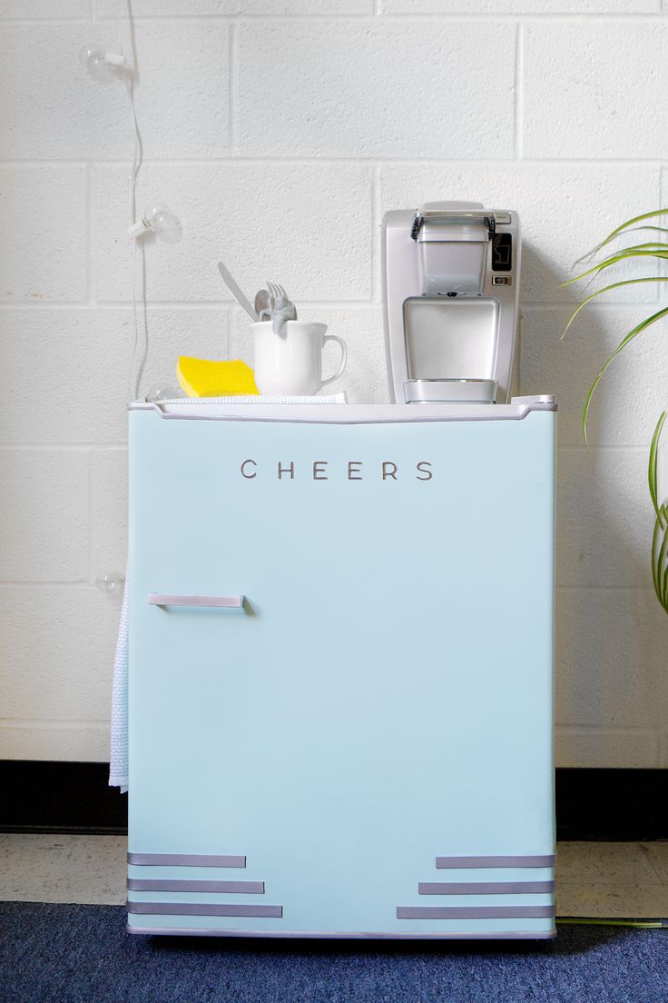 an old fashioned refrigerator sitting in front of a white brick wall next to a potted plant