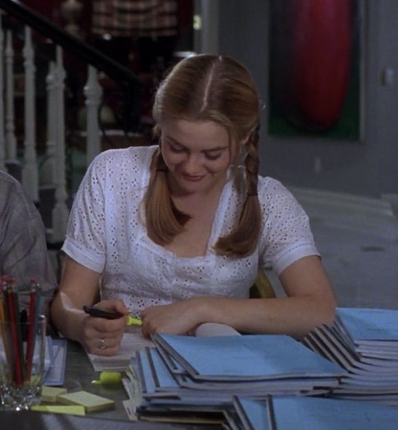 two people sitting at a table with papers and pens in their hands, one woman is typing on her cell phone