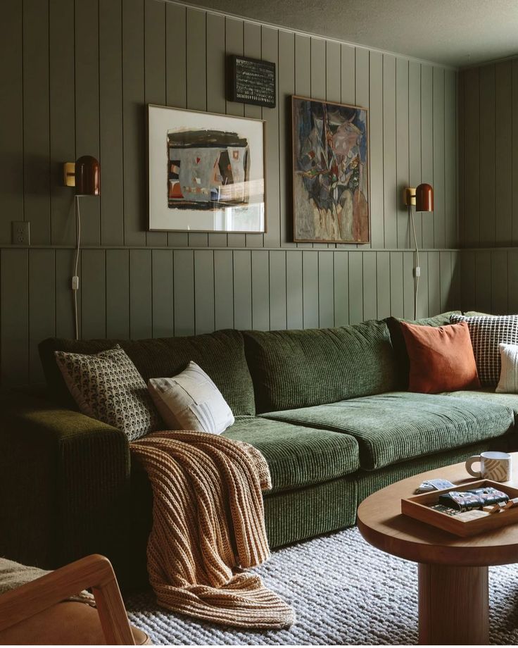 a living room filled with green couches next to a wooden table and two pictures on the wall