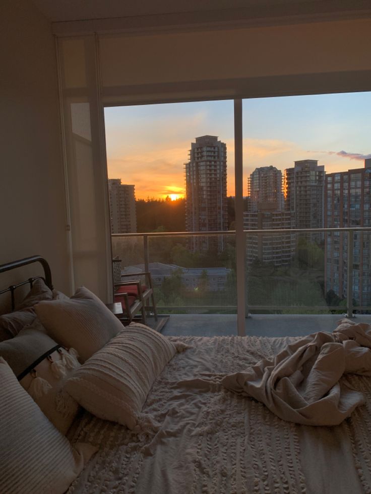 a bedroom with a view of the city at sunset or dawn from it's bed