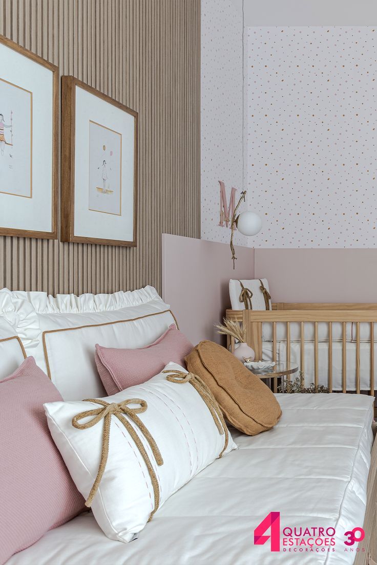 a baby crib with pink and white bedding in the corner next to two framed pictures on the wall