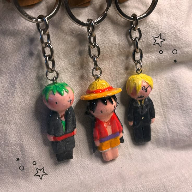 three key chains with small cartoon figures hanging from them on a white cloth covered surface