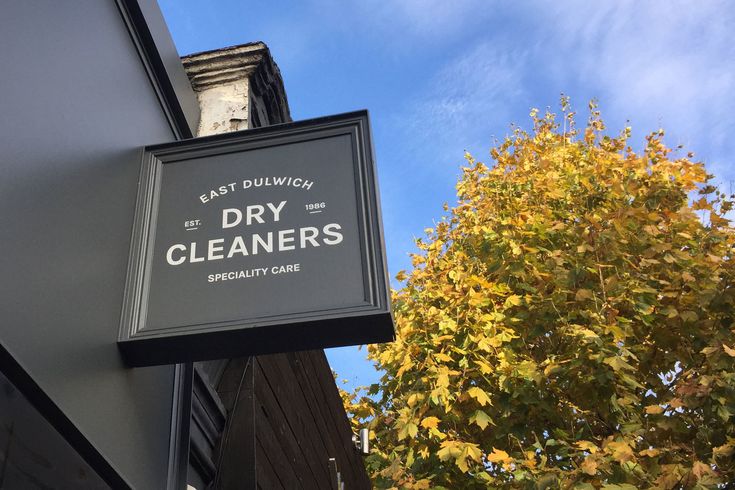 the dry cleaner's sign is hanging from the side of a building with trees in the background