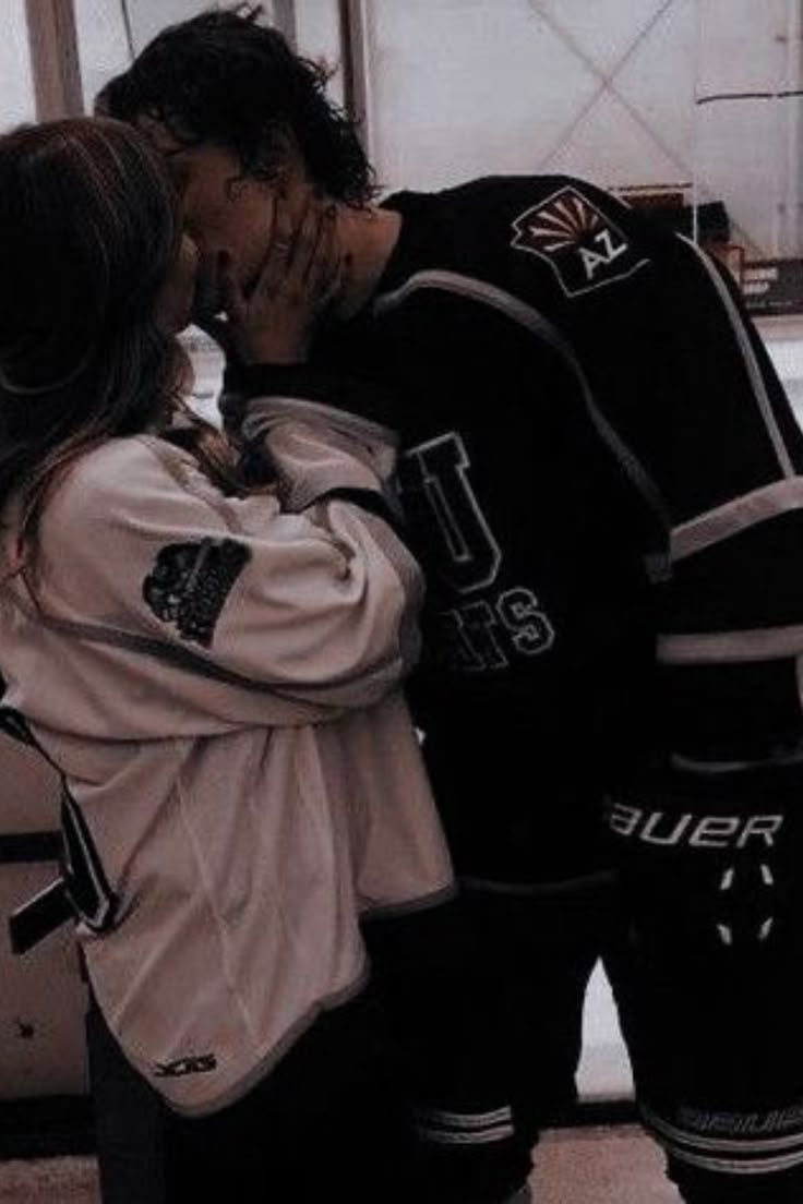 a man and woman kissing in front of an ice hockey goalie's net