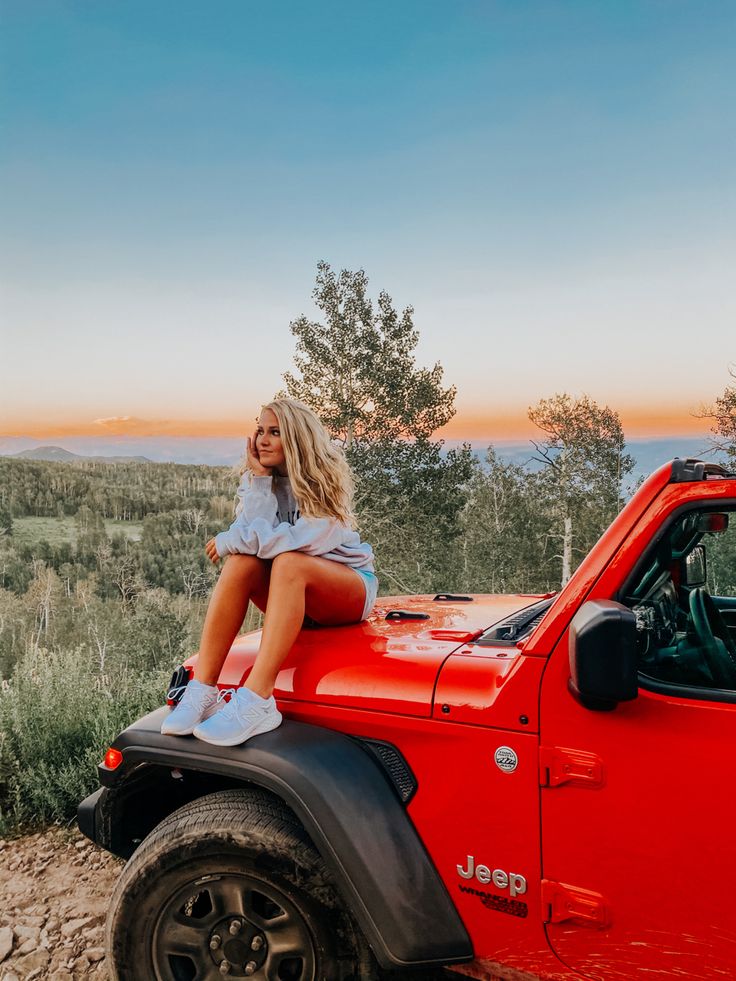 a woman sitting on top of a red jeep