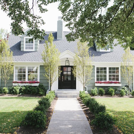 a gray house with white trim and two story windows on the front door is surrounded by greenery