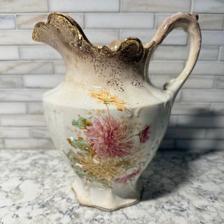 a white vase sitting on top of a marble counter next to a brick wall with flowers painted on it