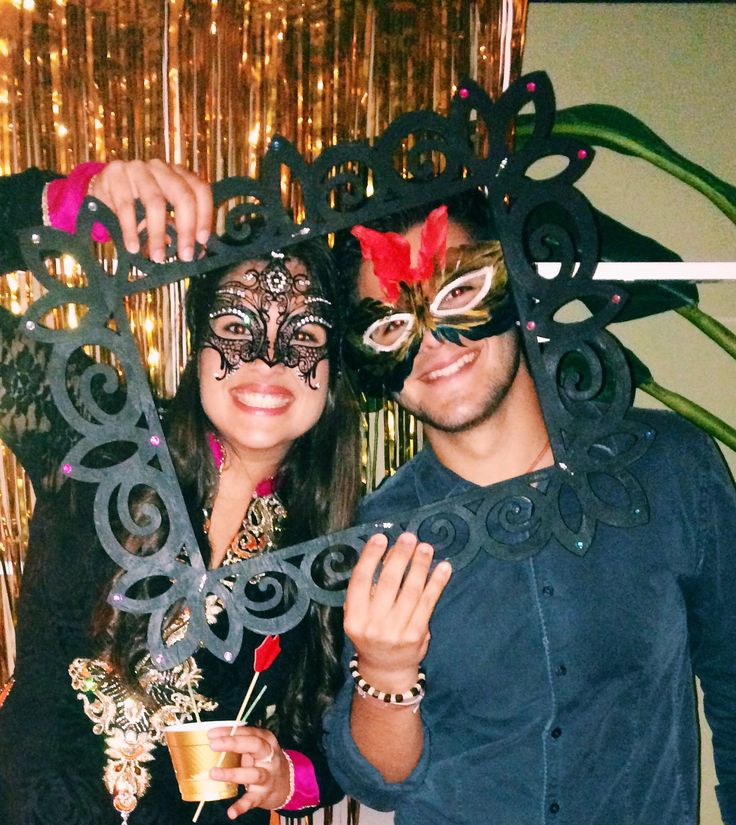 two people standing next to each other wearing masquerades and holding drinks in their hands