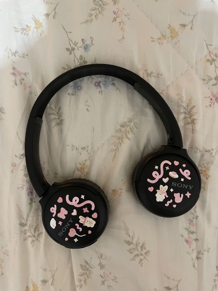 two black headphones with pink and white designs on them sitting on top of a bed