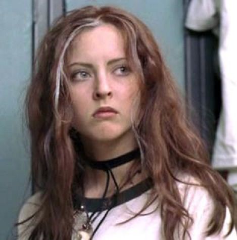 a woman with long hair wearing a choker and looking at the camera while standing in front of a mirror