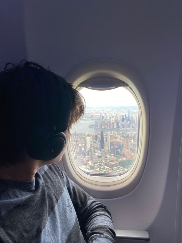 a person sitting in an airplane looking out the window at the city below and wearing headphones