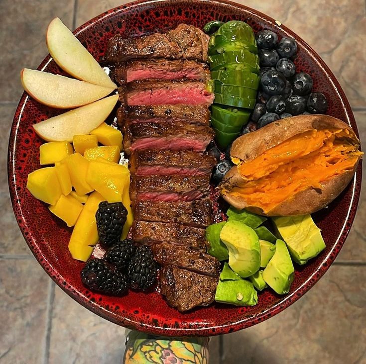 a red plate topped with meat, fruit and vegetables