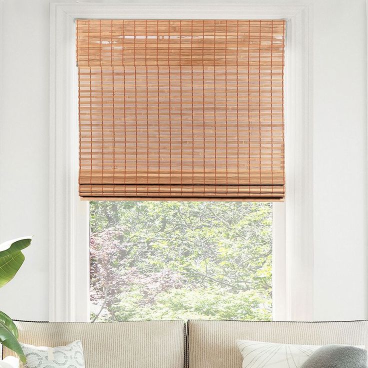 a living room with a couch and window covered in bamboo blind shades on the windowsill