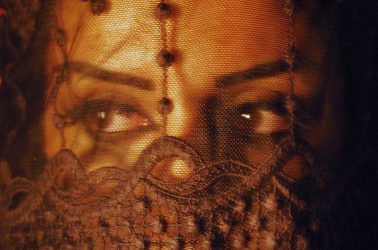 a woman's face is reflected in the mesh covering her eyes and headdress