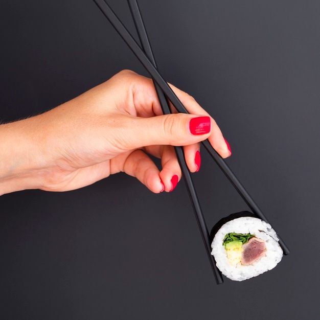 a woman's hand holding two chopsticks over a sushi roll