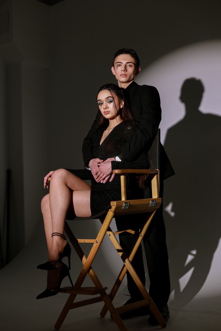 a man and woman sitting on a director's chair in front of a shadow