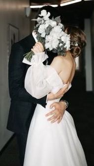 the bride and groom are hugging each other in their wedding day attire, dressed in black tuxedo with white flowers