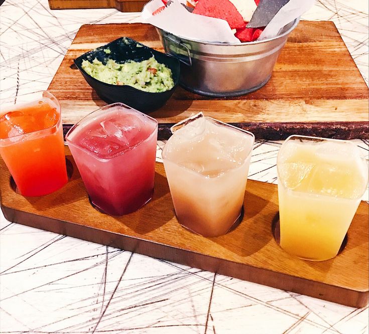 four different colored drinks on a wooden tray