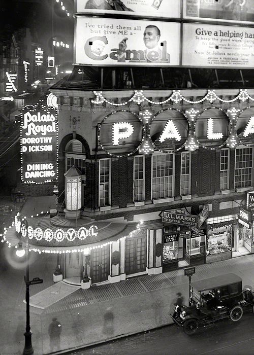 an old black and white photo of the outside of a building with neon signs on it