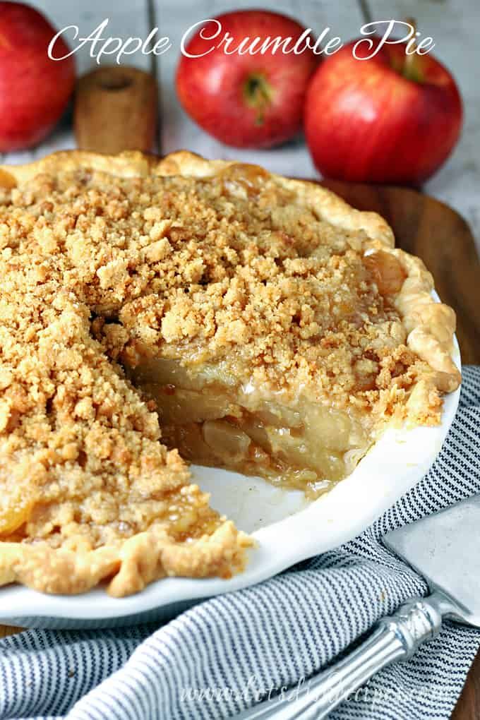 an apple pie on a plate with two apples in the background