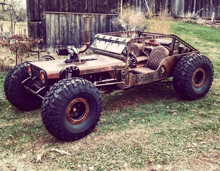 an old jeep is parked on the grass in front of a wooden fence and building